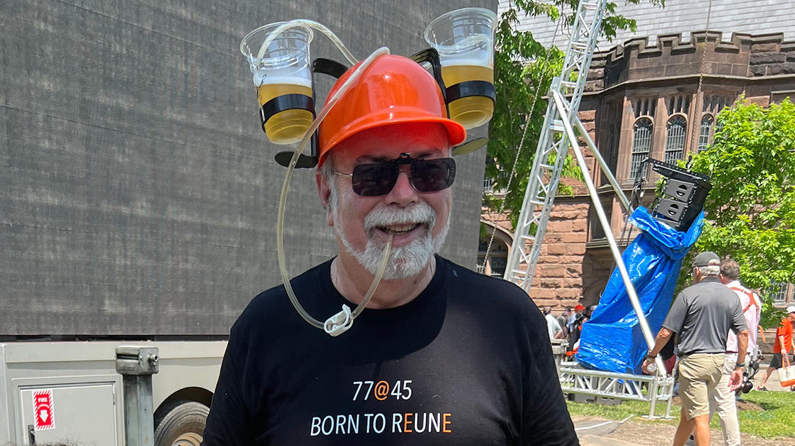 A man wears a hard hat with two cups of beer attached. His shirt reads "Born to Reune."