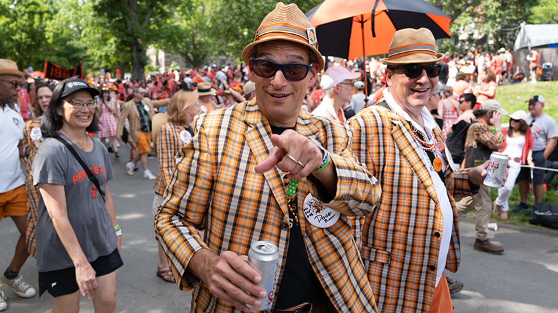 A man in an orange plaid blazer points to the camera during the P-rade.