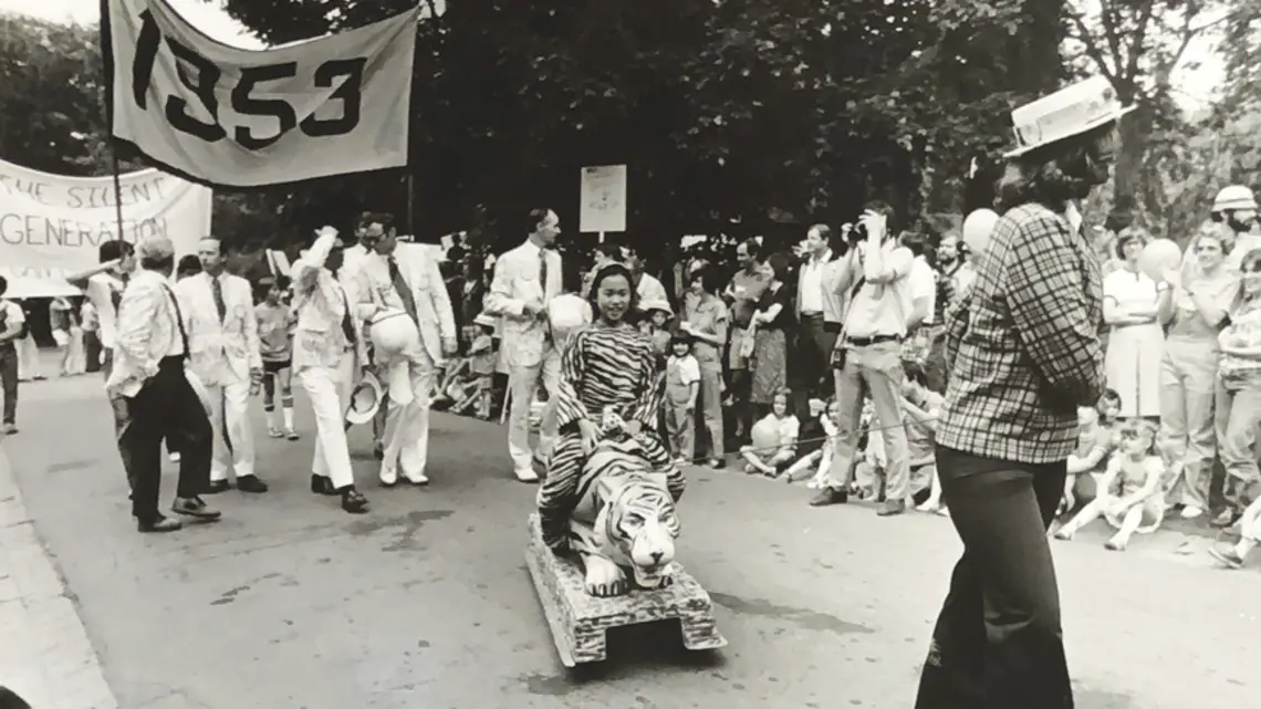 Black and white photo of the 1977 P-rade featuring a little girl dressed in a tiger costume being pulled by a female marcher in front of the Class of 1953 marching