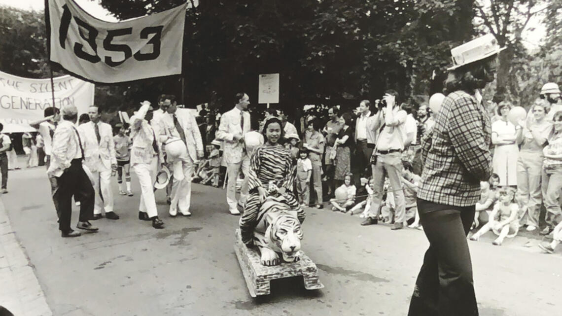 Black and white photo of the 1977 P-rade featuring a little girl dressed in a tiger costume being pulled by a female marcher in front of the Class of 1953 marching