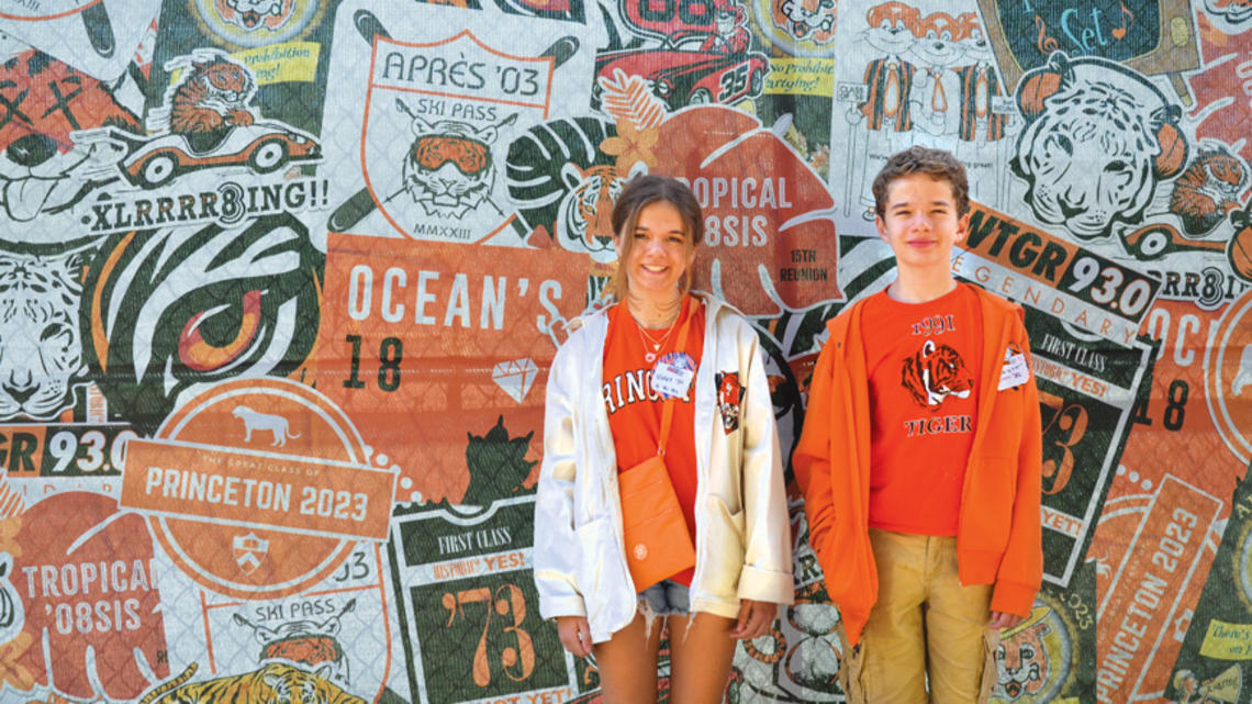 RG_Kids Experience.jpg Violet and Everett Dutton standing in front of a collage of Class logos at Reunions 2023