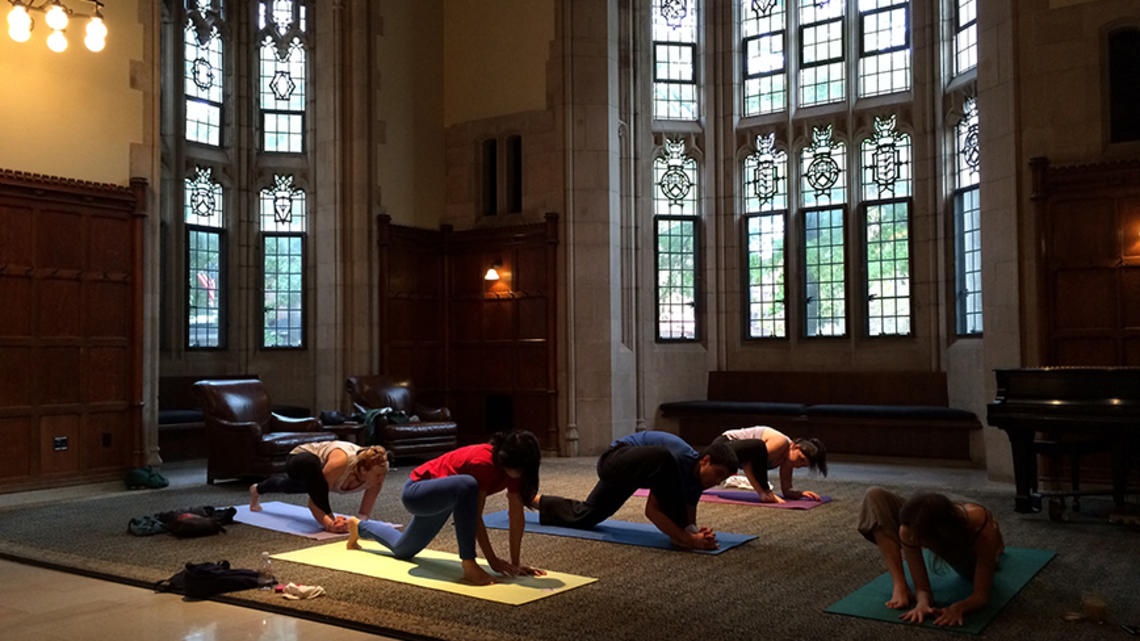 Yoga.jpg Five people practice yoga in a dim room with Gothic windows.