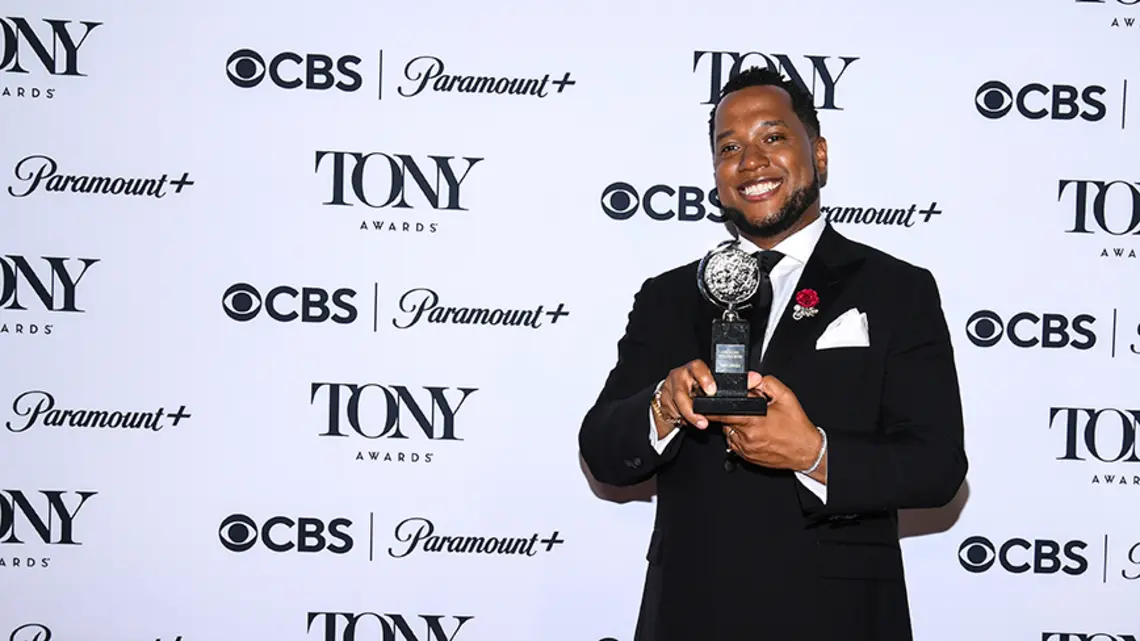 Branden Jacobs-Jenkins ’06 holds his Tony award in front of a step-and-repeat covered with logos for CBS, Paramount+, and the Tony Awards.