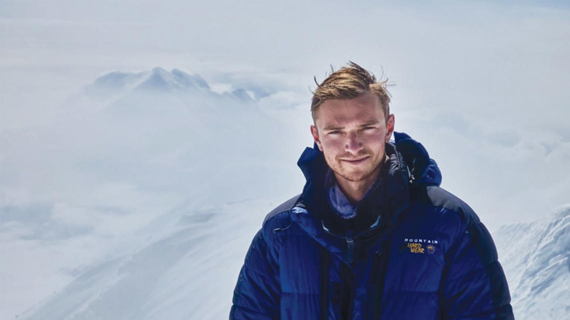 Ben Weissenbach in a blue puffer jacket on top of a snow covered mountain