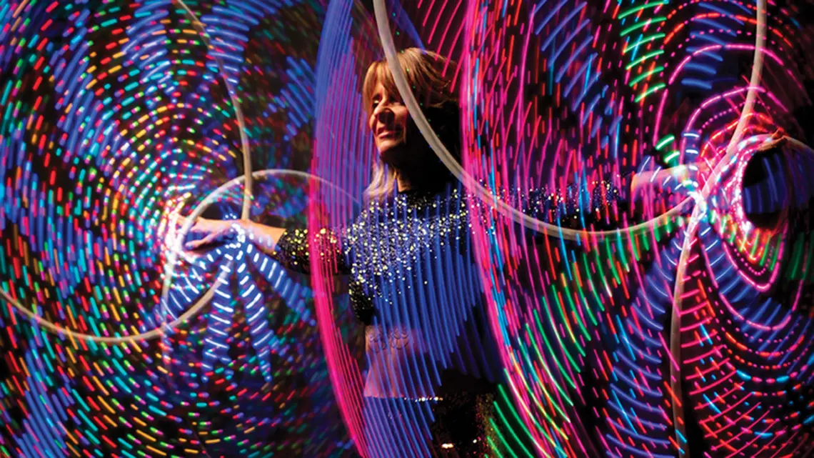 A woman spins colorful illuminated hula hoops around her wrists and ankles simultaneously. 