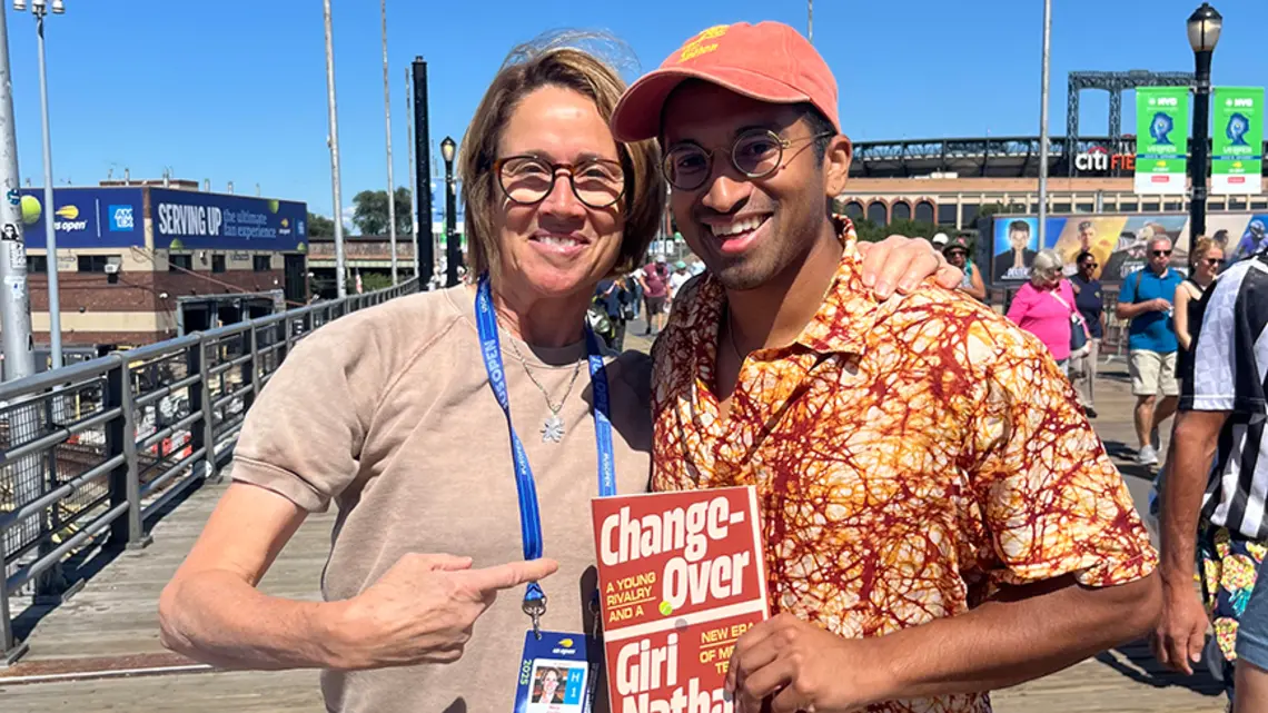 TOW_GiriNathan.jpg Two people on a sunny boardwalk holding a copy of the red book "Changeover."