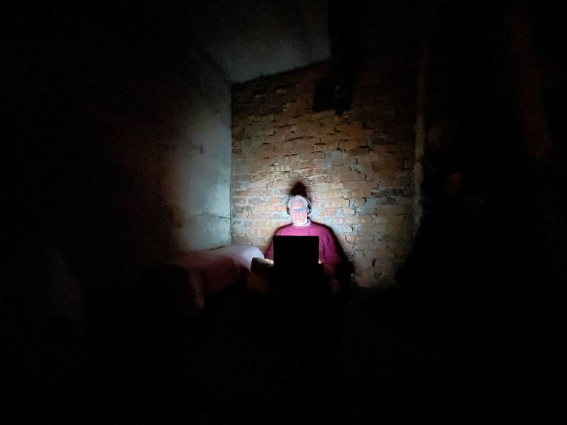 Frank Langfitt ’86 works in a bomb shelter in central Ukraine, the light from his laptop illuminating him and the brick wall behind him.