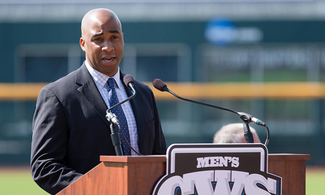 Damani Leech ’98 speaks at a podium with a baseball field in the background.