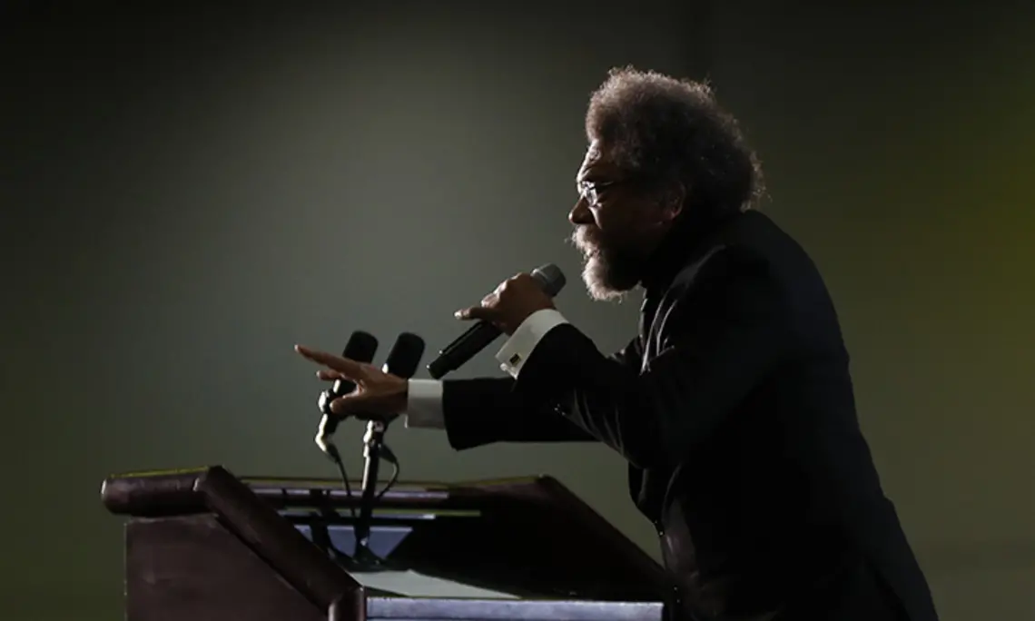 This is a photo of Cornel West, in profile, speaking at a podium.