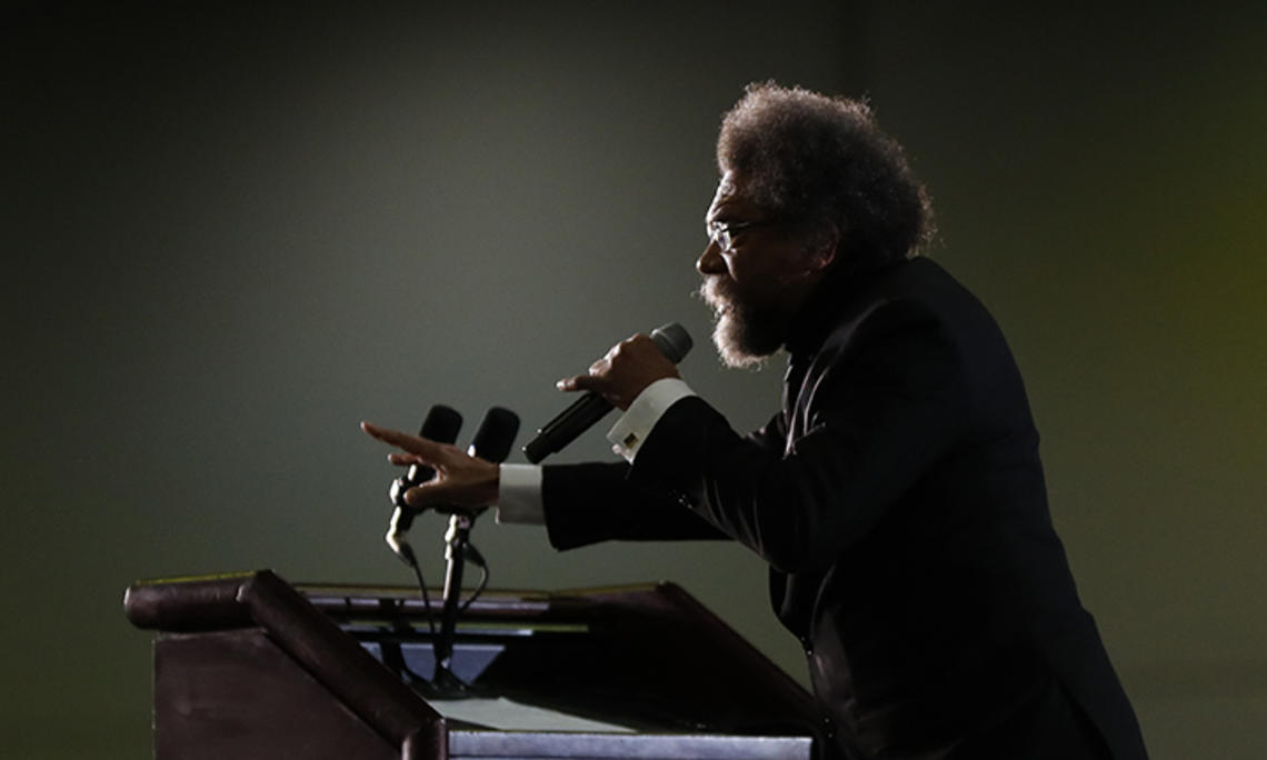 This is a photo of Cornel West, in profile, speaking at a podium.