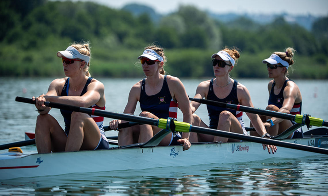 Four rowers at rest in a rowing shell on the water. Claire Collins is at left.