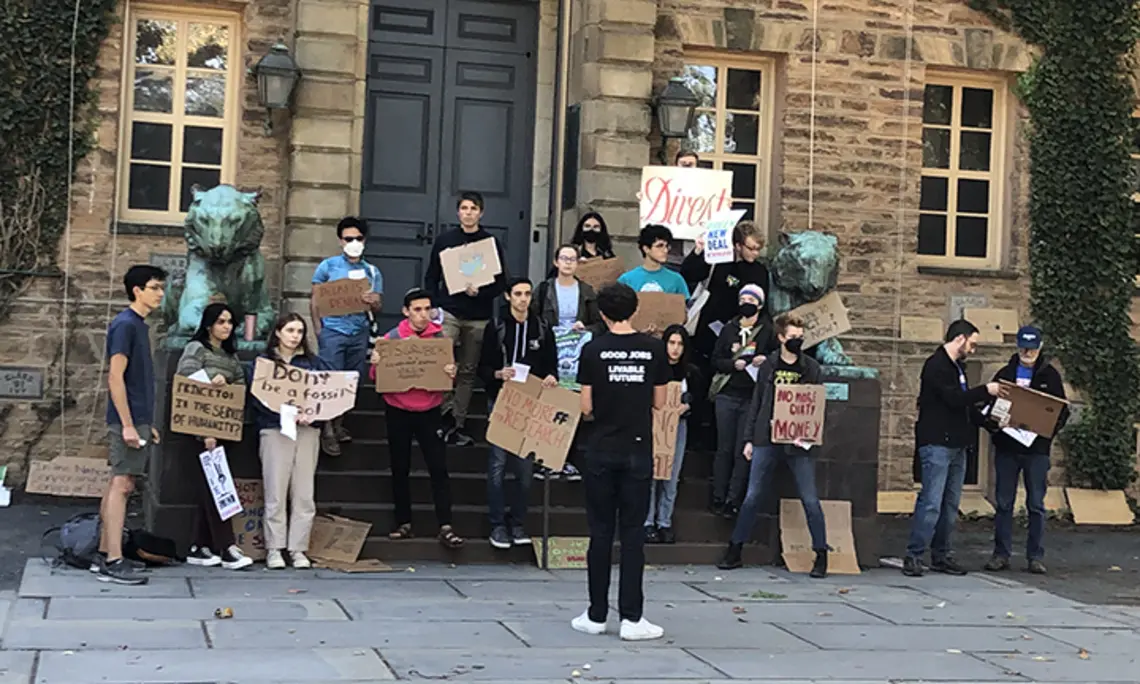 Students with Divest Princeton hold signs in front of Nassau Hall, made of cardboard and showing their support for Princeton divesting from fossil fuels.