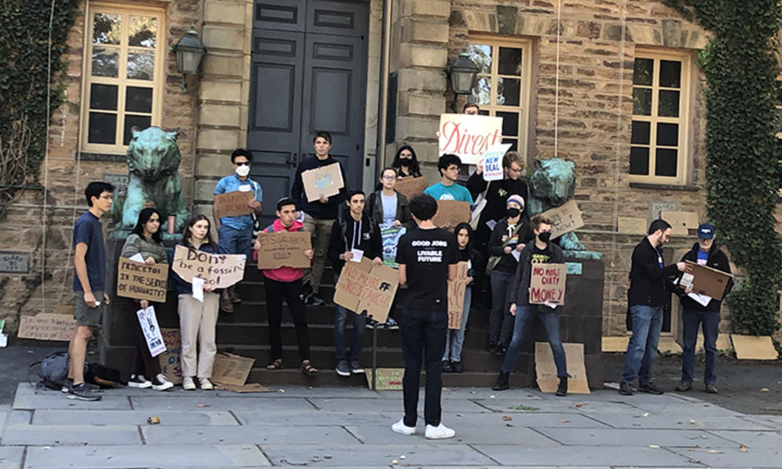 Students with Divest Princeton hold signs in front of Nassau Hall, made of cardboard and showing their support for Princeton divesting from fossil fuels.