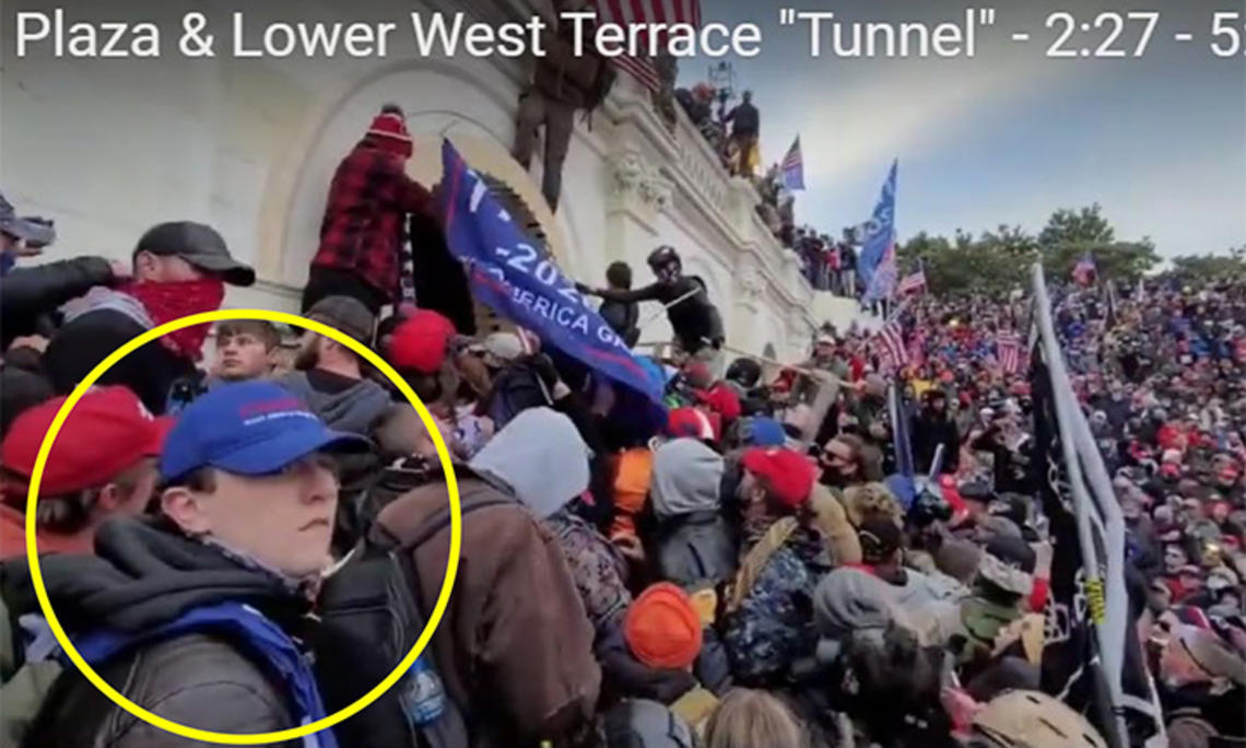 Giberson_figure16.jpg A yellow circle has been drawn about a boy in the foreground, wearing a blue baseball cap. In the background a crowd climbs over the wall around the Capitol.
