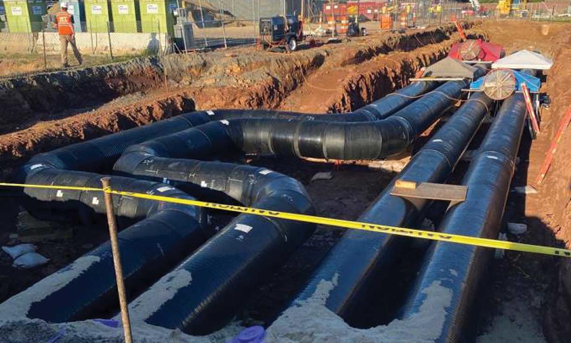 This is a photo of the thermal piping installed near Jadwin Gym — four big black pipes down in a dug-out area of reddish dirt..