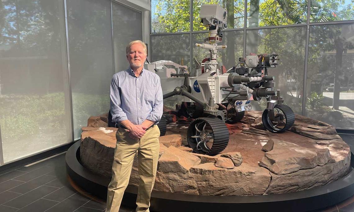 Photo of Chad Edwards ’79 in front of a full-scale model of the Perseverance rover