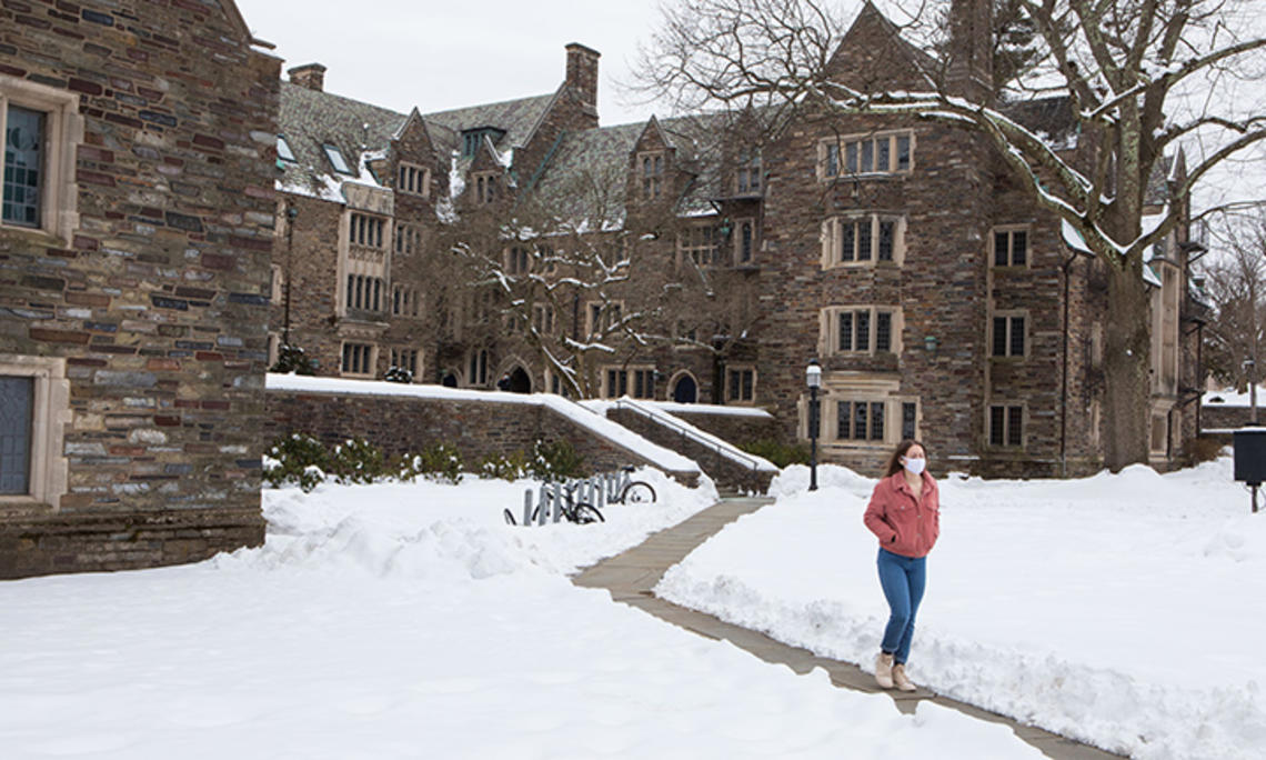 A masked student walks across campus, on a path cut through the snow, in 2021.