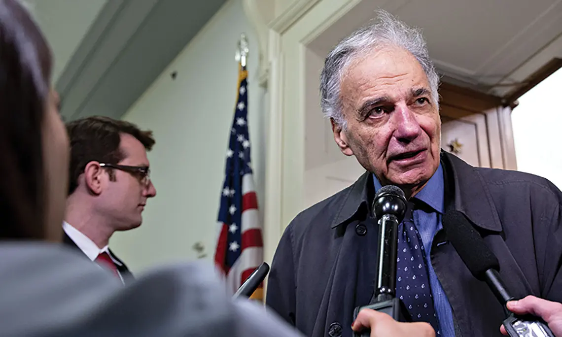 Ralph Nader speaks into a microphone to the press.