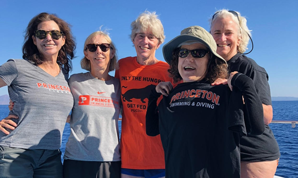 Five women standing on a boat wear various Princeton T-shirts.