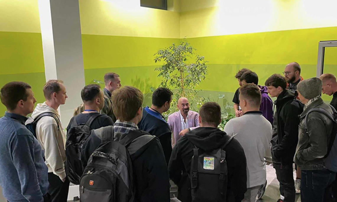 David Spergel ’82 talks to a room full of young men. A small tree is behind him and the walls are shades of green.