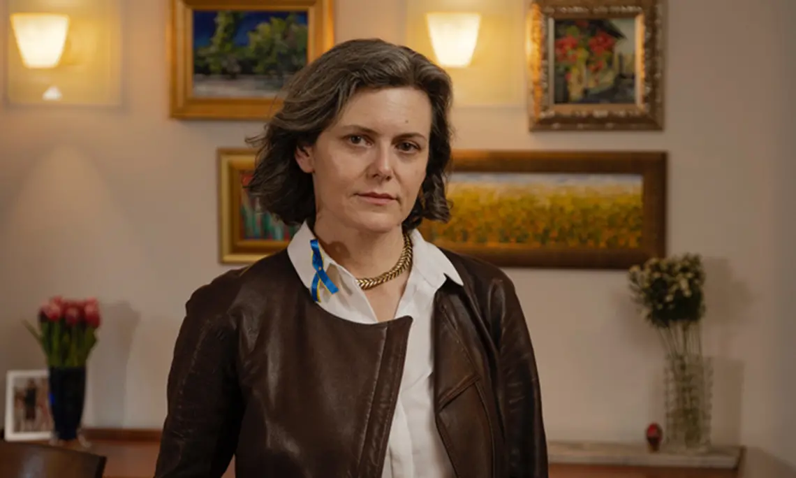 This is a photo of Dora Chomiak ’91 in front of a wall hung with paintings.