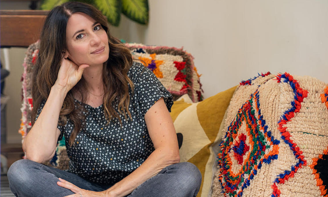 This is a photo of Julia Storm ’96 sitting on a couch with a couple of crocheted blankets on it.