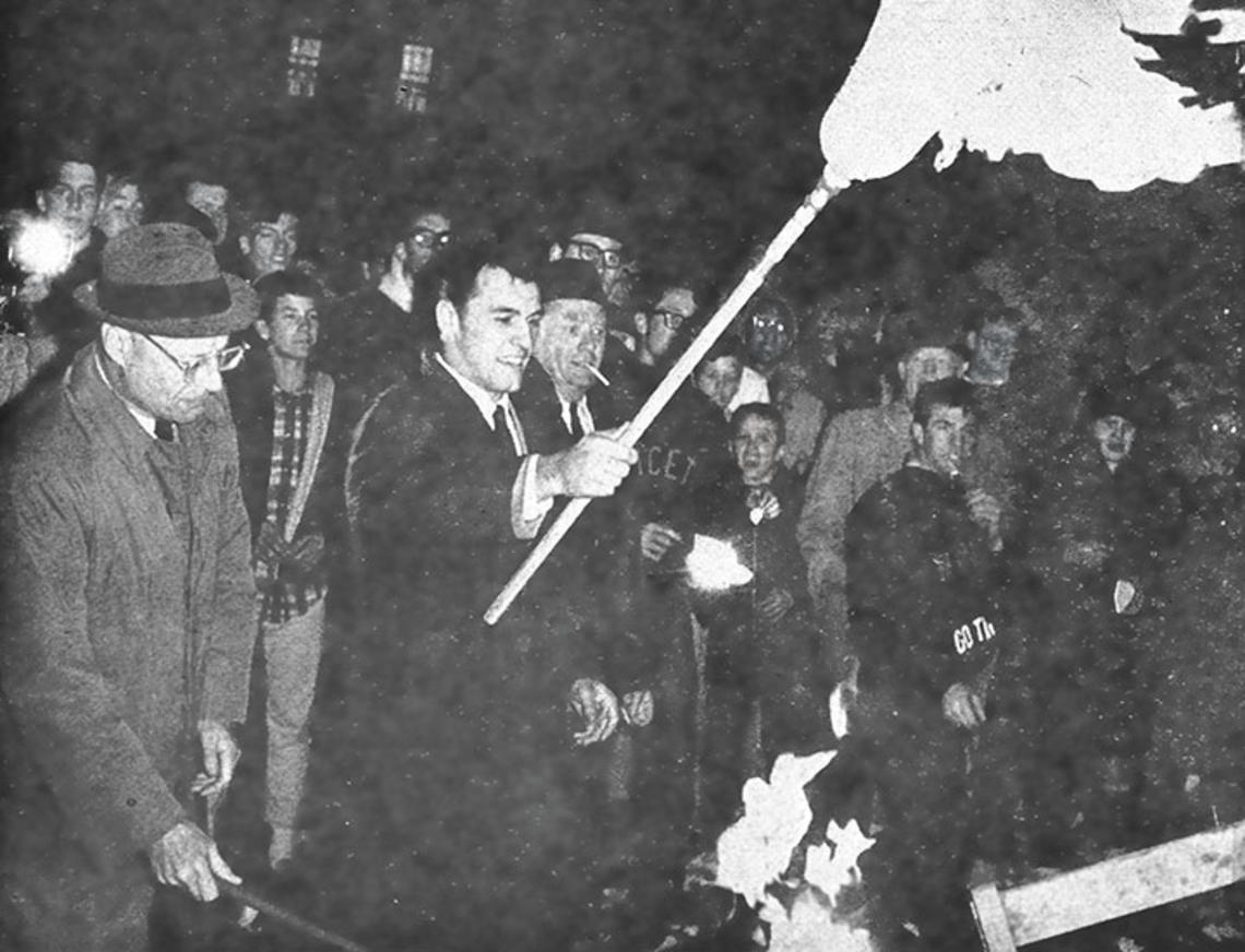 All-American Cosmo Iacavazzi ’65 *68 lights the bonfire, with coach Dick Colman (in glasses) by his side.