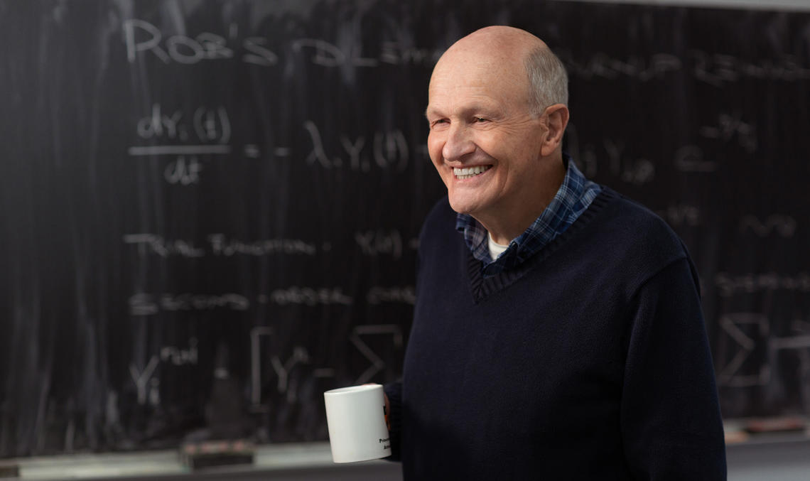 This is a photo of Frank N. von Hippel in front of a chalkboard. He's holding a coffee mug.