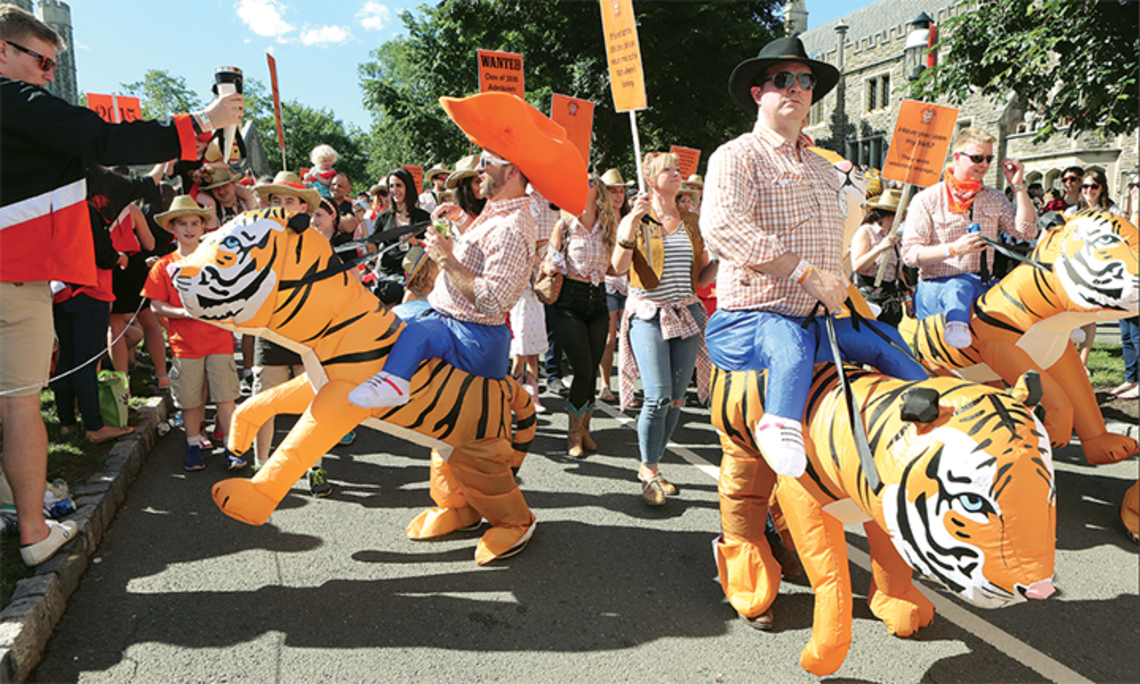 This is a photo from the P-rade in 2017 of the Class of 2002 riding inflatable tigers. One is wearing an orange cowboy hat.