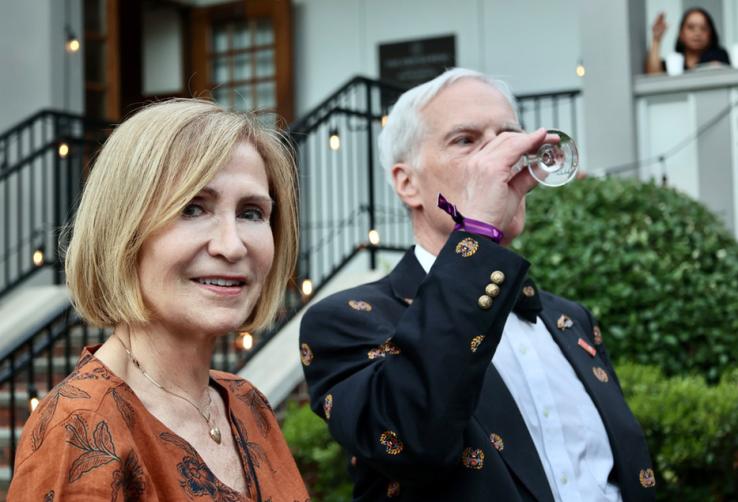 A man drinks a glass of wine; a woman smiles for the camera.