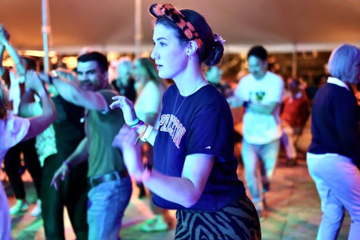 A woman dances in a tent while wearing a tiger ears headband. 