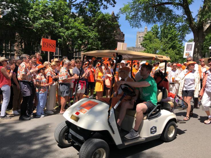 A student drives a member of the Old Guard in a golf cart.