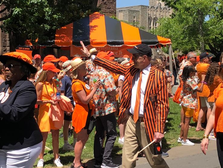A man wearing a black and orange striped jacket waves to people during the P-rade.