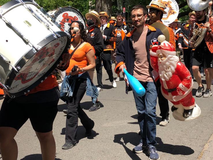 Band members march in the P-rade; one holds a baseball bat and a plastic Santa Clause.