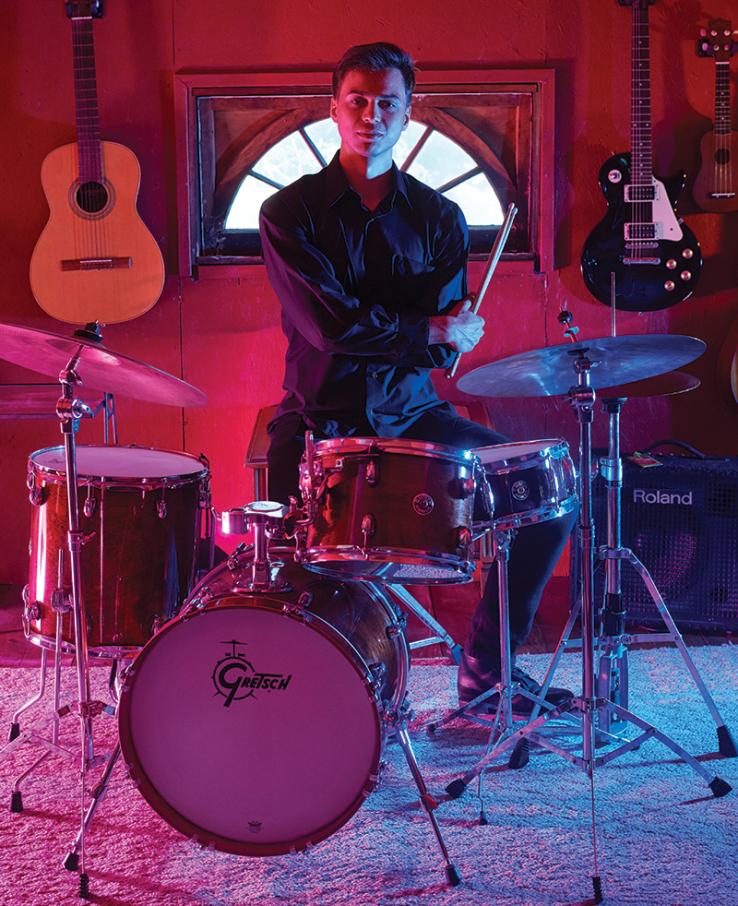 Calvin Van Zytveld ’19 sits at a drum set in a darkened room lit by red light.