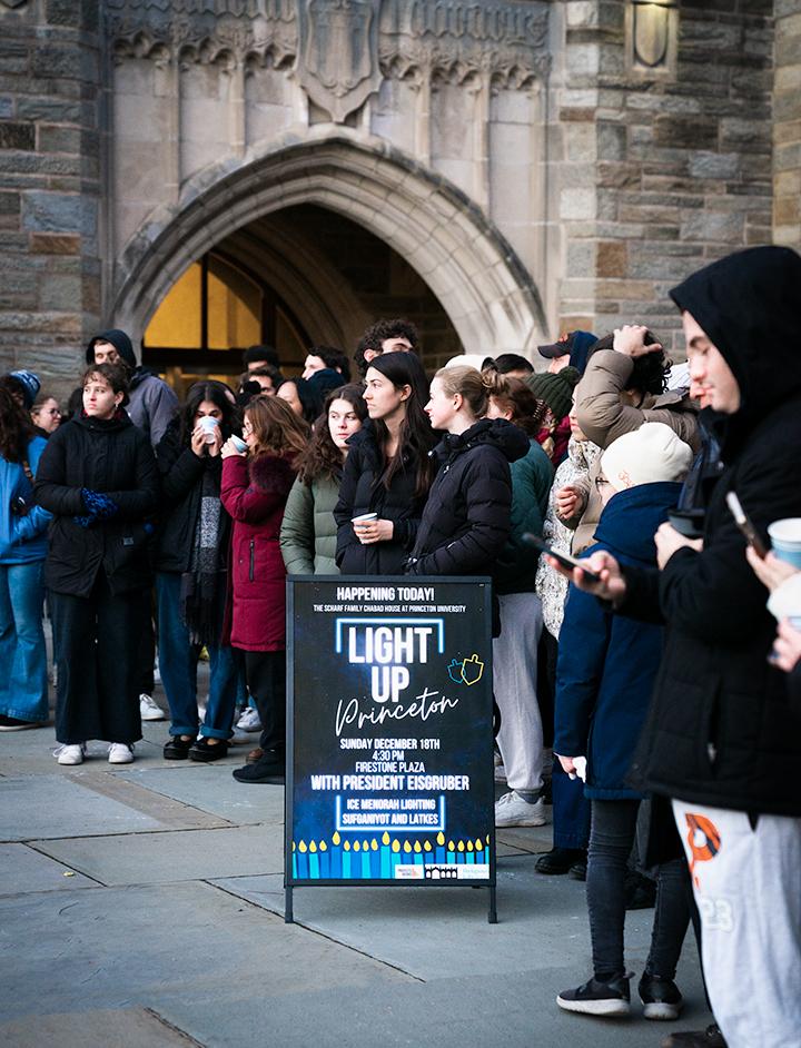 Students gather behind a small sign for the event reading "Light Up Princeton"