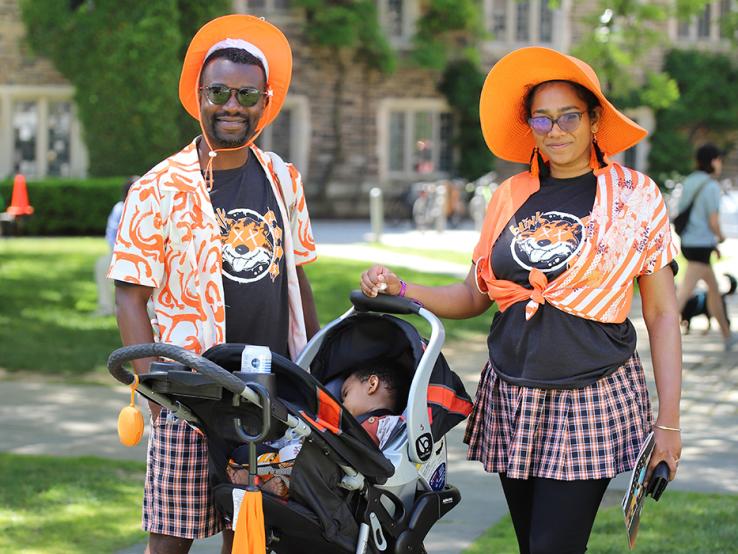 Two people wearing orange hats next to a sleeping baby in a stroller.