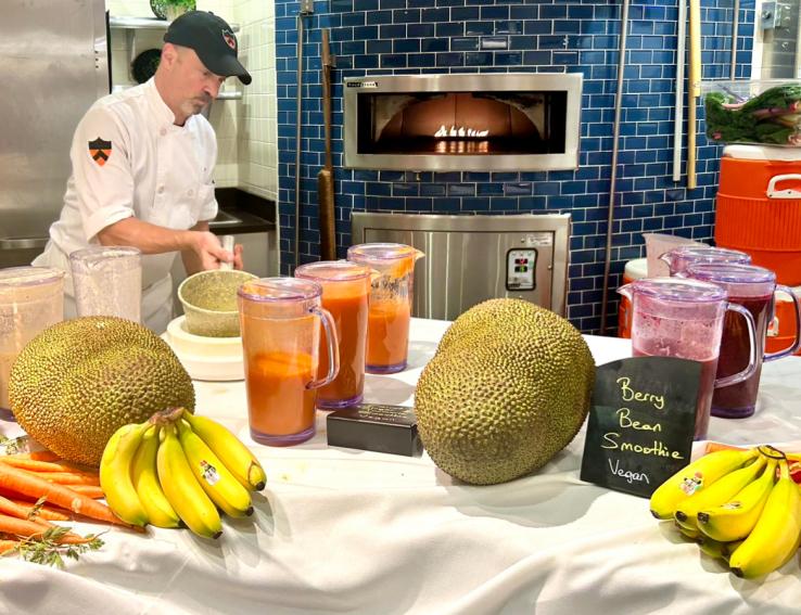 Dining staff prepare vegan berry bean smoothies on a table with bananas and jackfruit.