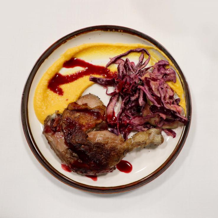 This is a close up photo of a plate of food that looks like a chicken leg, red cabbage and polenta with a red sauce drizzled on top.
