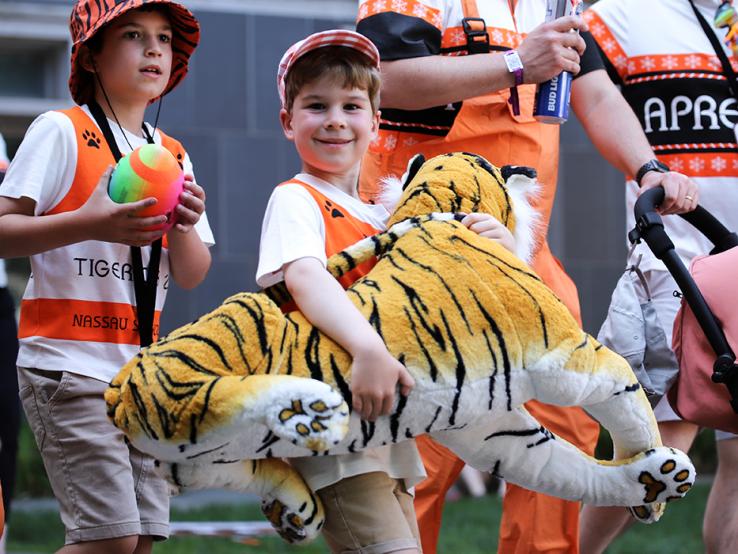 A kid carries a big plush tiger.