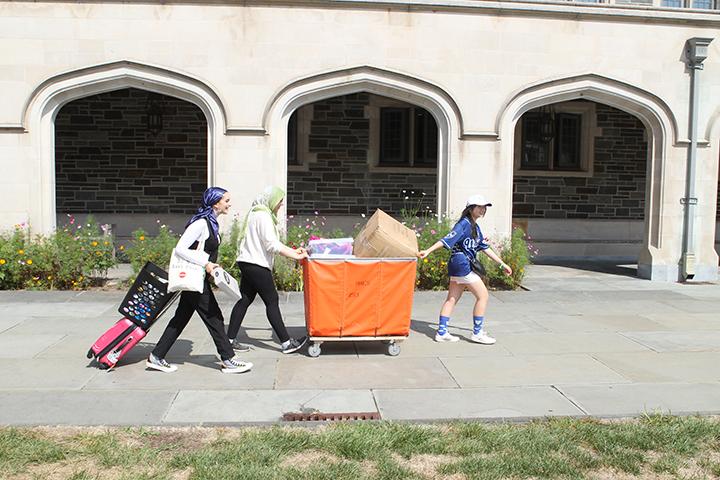 Three women push and pull a large orange bin.