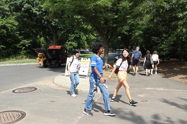 Students walk across a street with trees in the background.