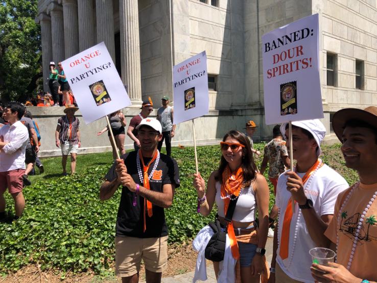 Alumni hold signs reading, "Orange U Partying?" and "Banned: Dour Spirits!"