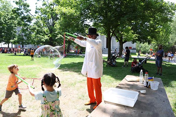 A man blows giant bubbles for two children with a rope-based bubble wand.
