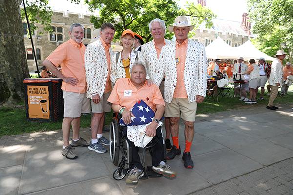 Five friends stand behind a man in a wheelchair holding a folded American flag.