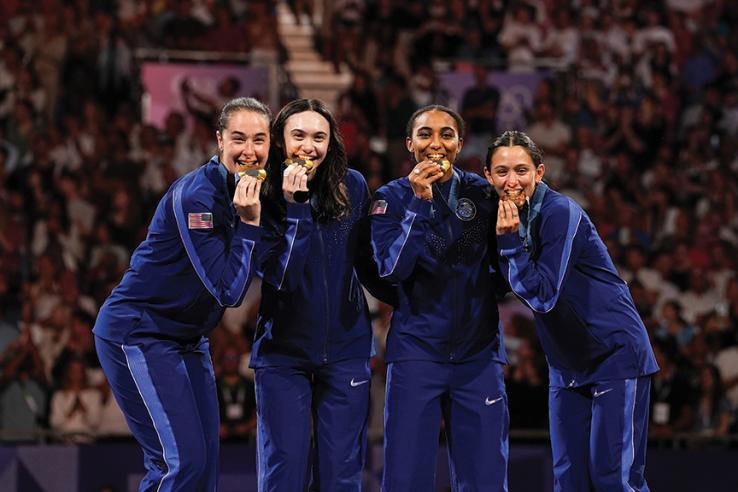 Four women in blue outfits bite into gold Olympic medals.