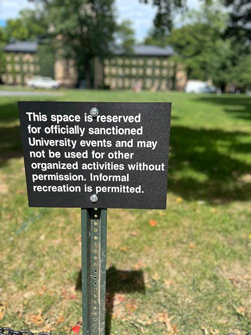 A small metal sign in front of Cannon Green reads: This space is reserved for officially sanctioned University events and may not be used for other organized activities without permission. Informal recreation is permitted.