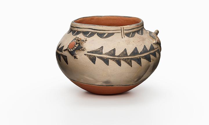 A terracotta pot with two clay turtles sculpted on it in relief, painted black and white.