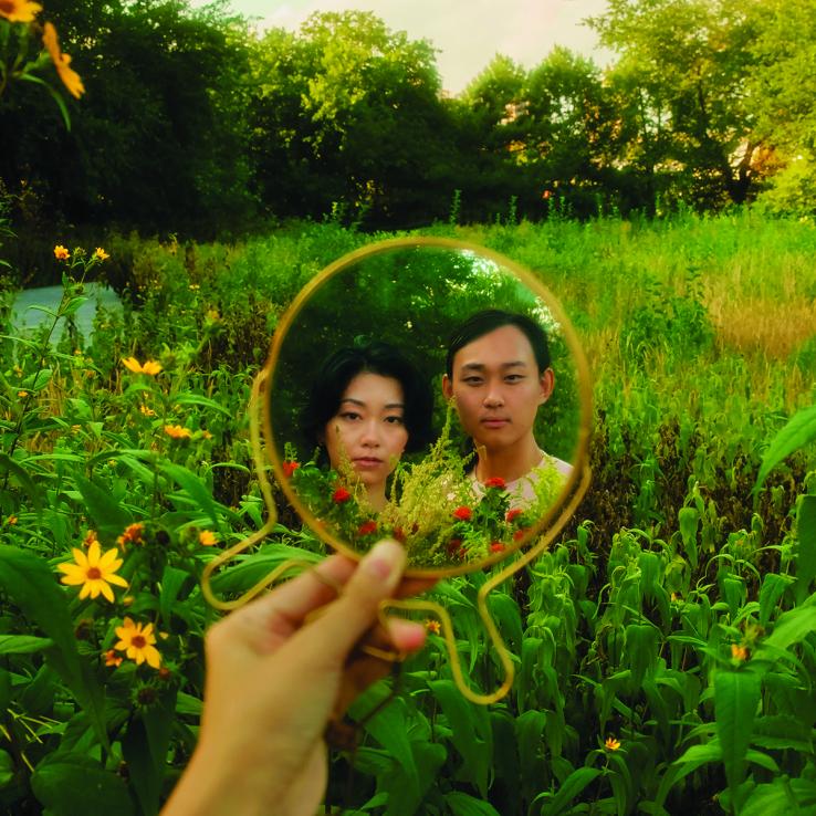 Two people in a field, reflected in a round mirror.