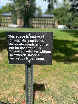 A small metal sign in front of Cannon Green reads: This space is reserved for officially sanctioned University events and may not be used for other organized activities without permission. Informal recreation is permitted.